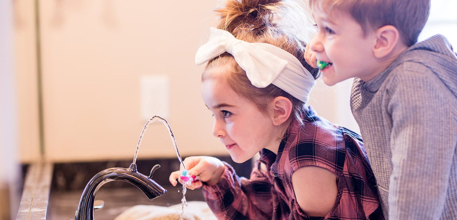 Two young children brushing teeth with Nasoni faucet