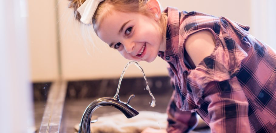 Young girl smiling at camera while drinking from Nasoni faucet